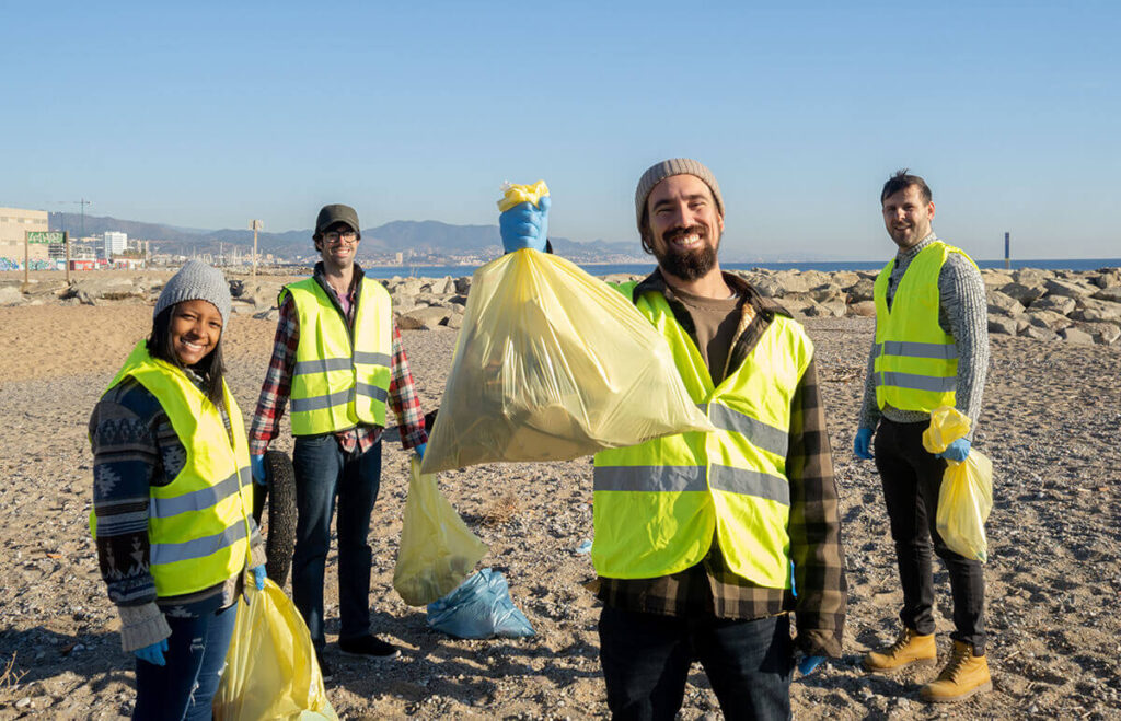 Volunteers in safety vests on beach picking up litter